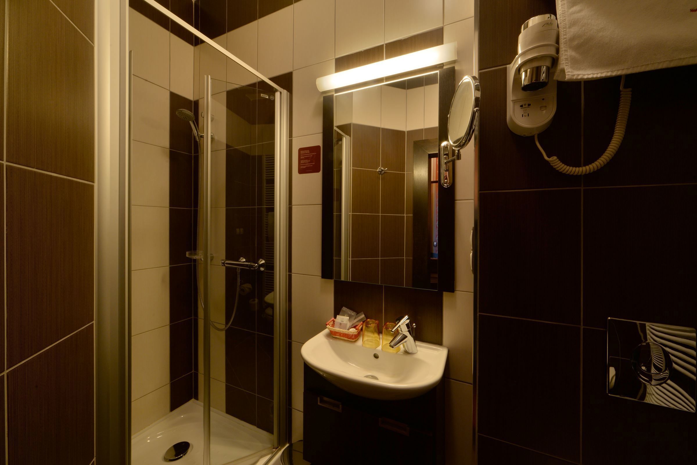 Een badkamer met een douchecabine van glas, een wastafel met toiletartikelen en een aan de muur bevestigde haardroger.