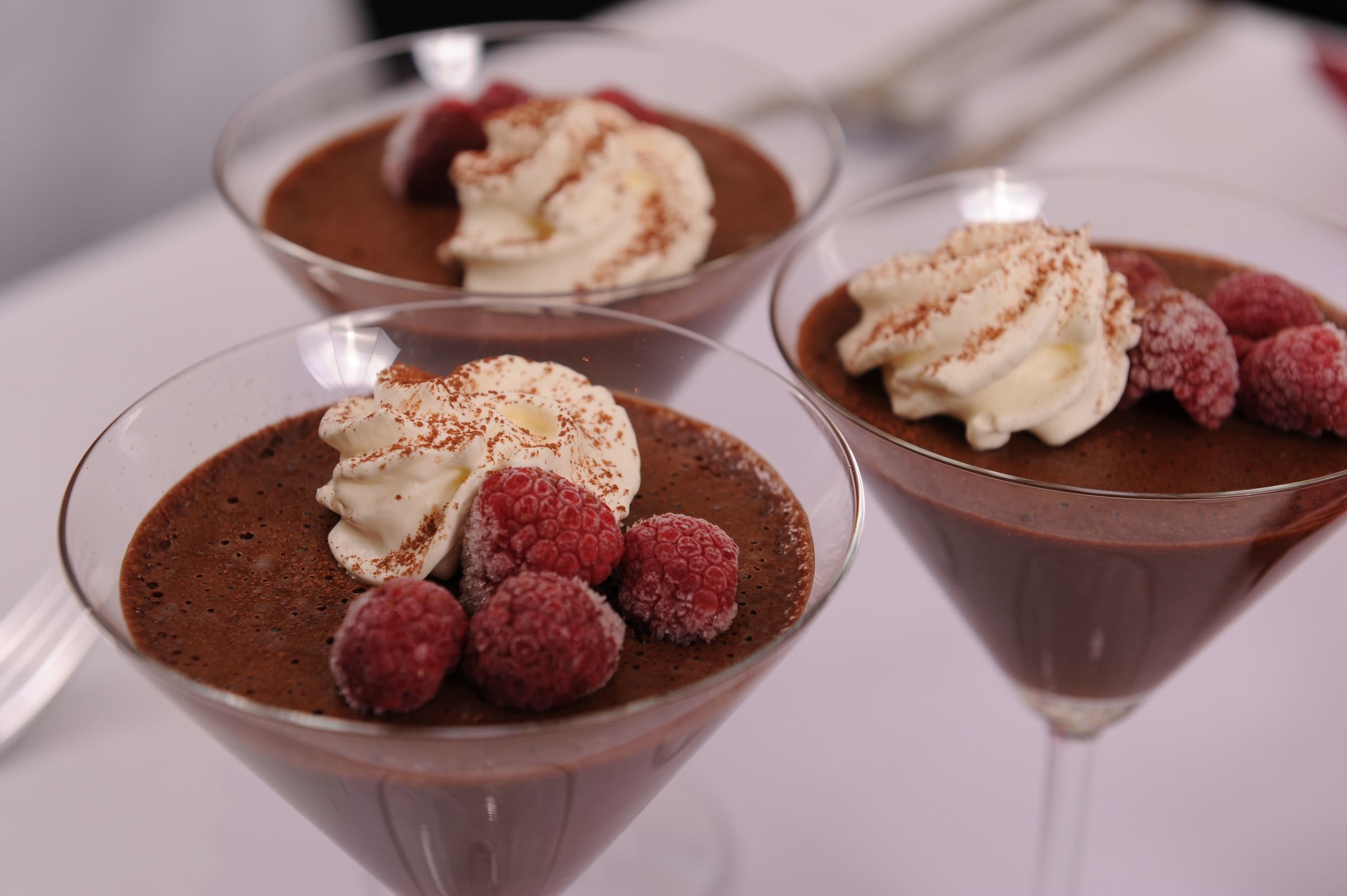Three dessert glasses with chocolate mousse, whipped cream, and raspberries.
