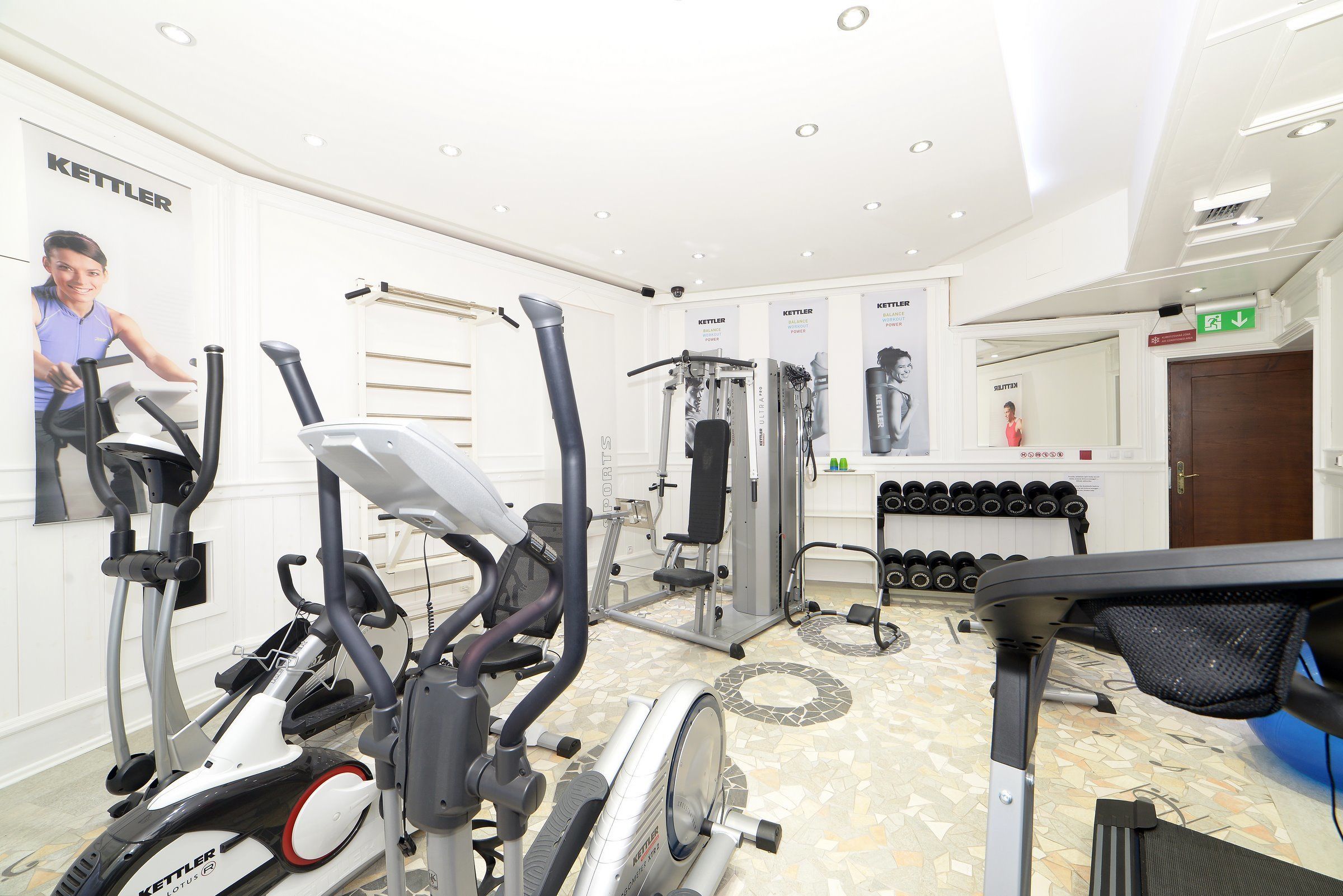 Ein Fitnessstudio mit verschiedenen Trainingsgeräten, darunter Laufbänder, Ergometer und Kraftgeräte.