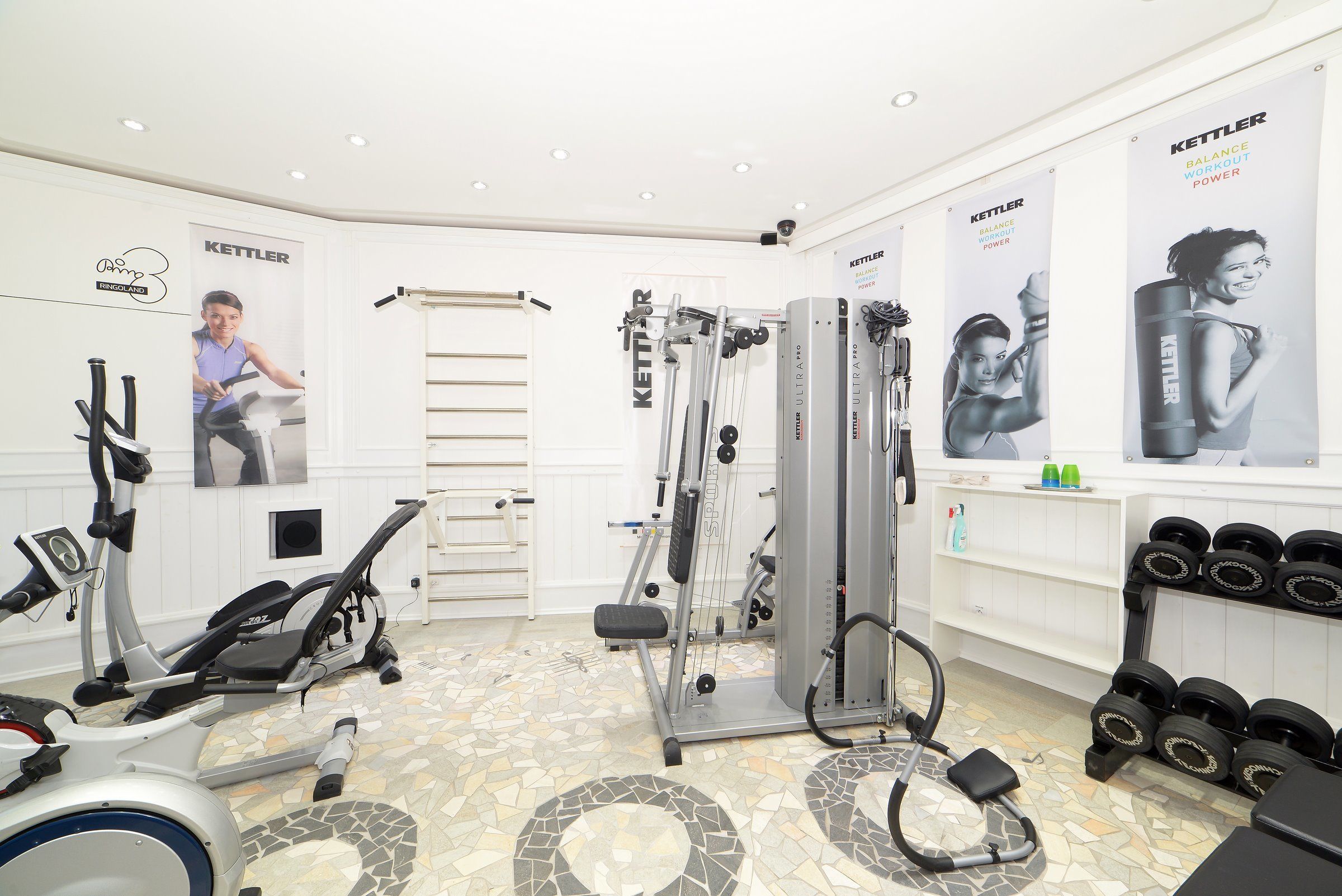 A gym with exercise equipment, a wall with posters, and a tiled floor.