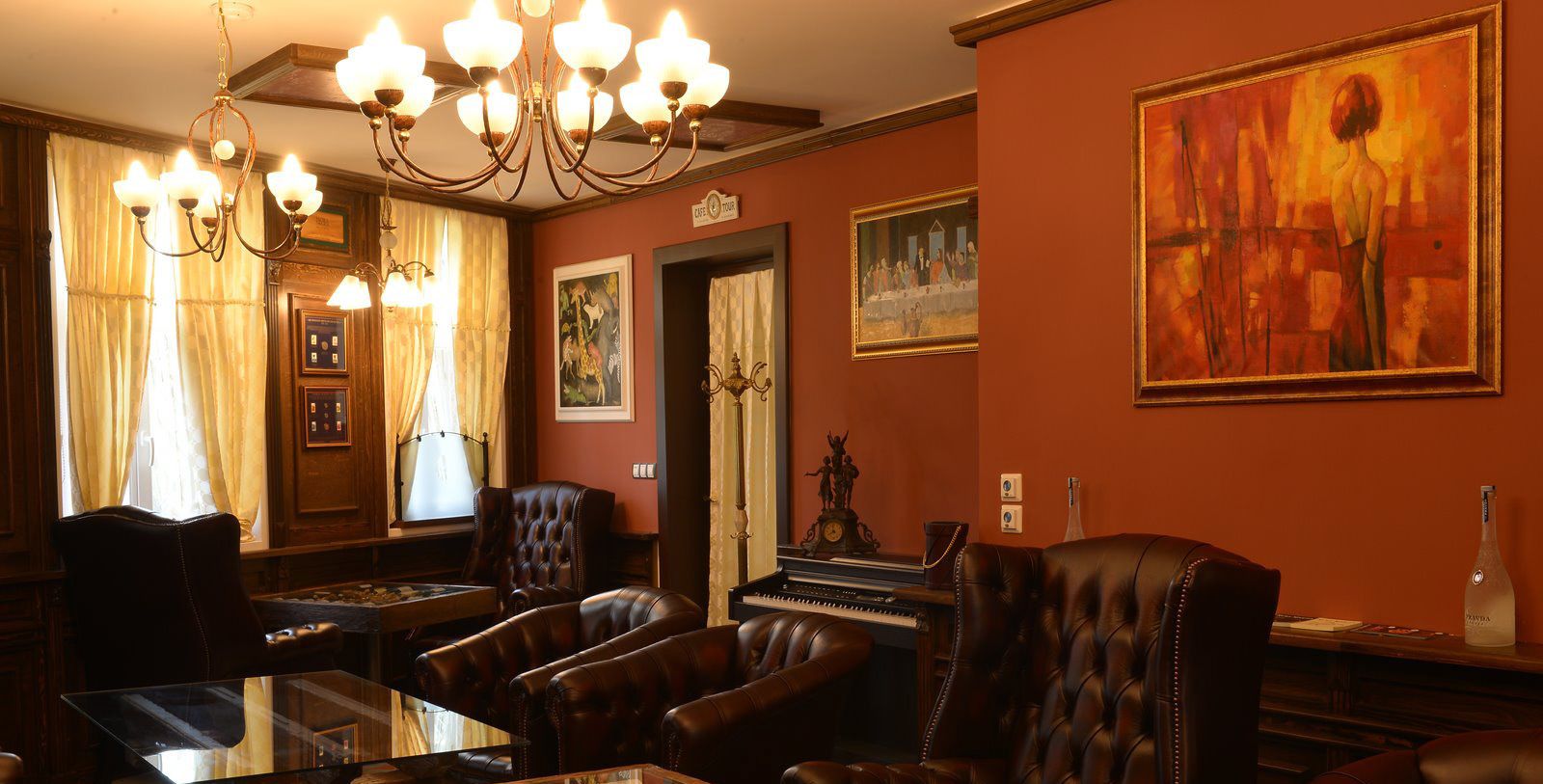 A room with a piano, leather chairs, a glass table, and a chandelier.