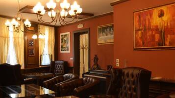 A room with a piano, leather chairs, a glass table, and a chandelier.