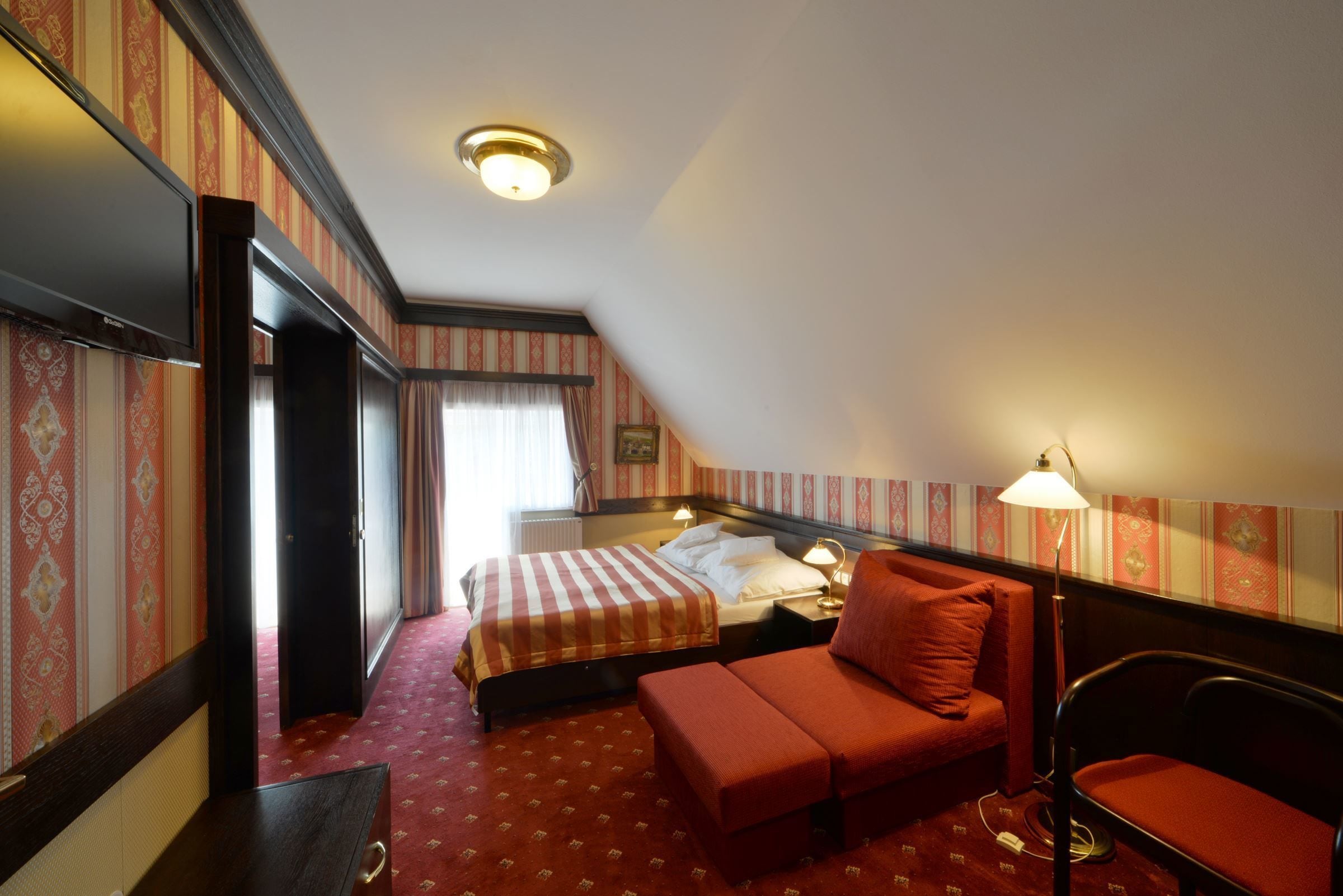 Quarto de hotel com cama, sofá, escrivaninha e luminária.