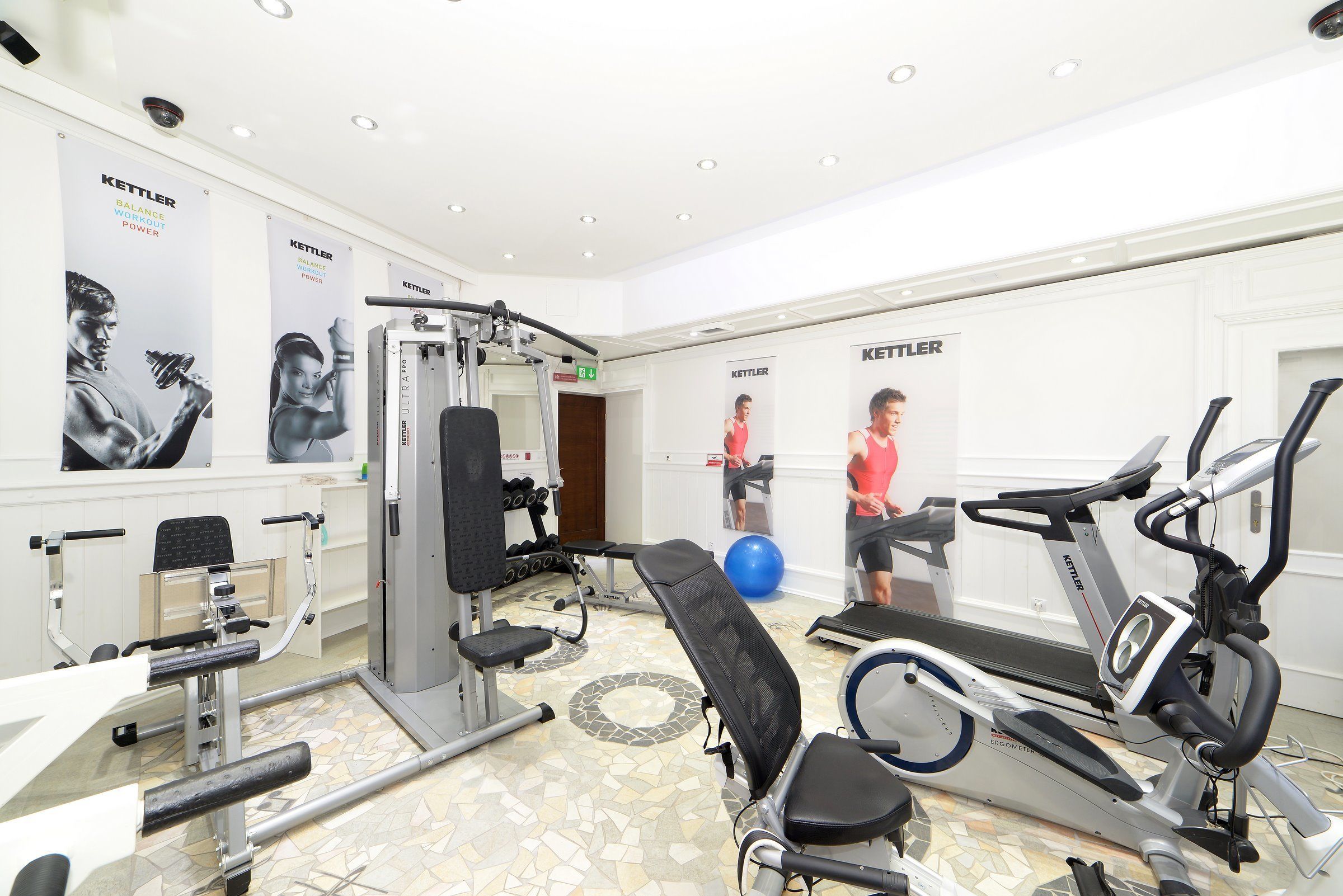Un gimnasio con varios equipos de ejercicio, incluyendo una prensa de banca, una cinta de correr y una bicicleta estática.