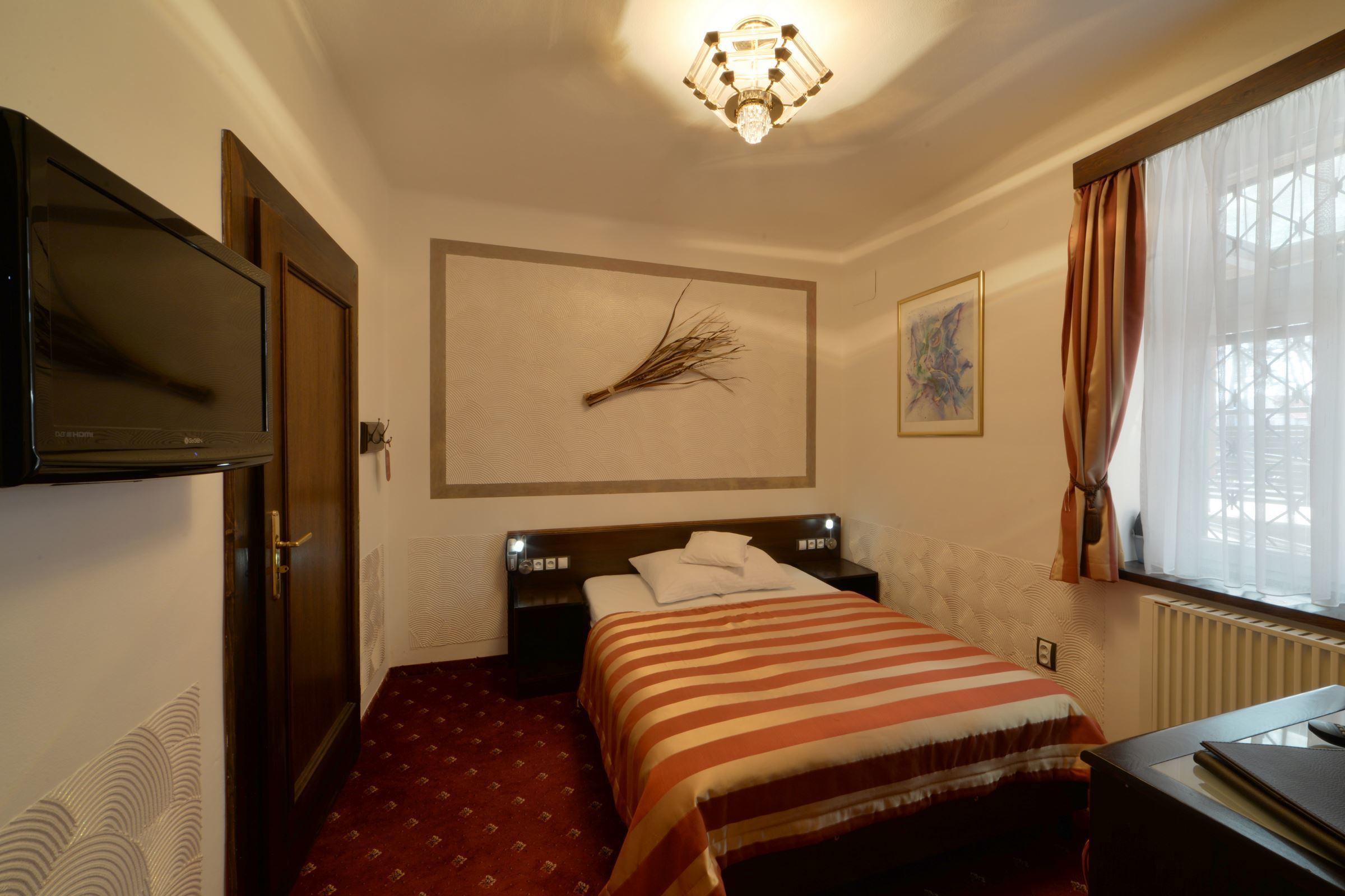 A hotel room with a bed, a desk, a television, a window with curtains, and a wall-mounted artwork.