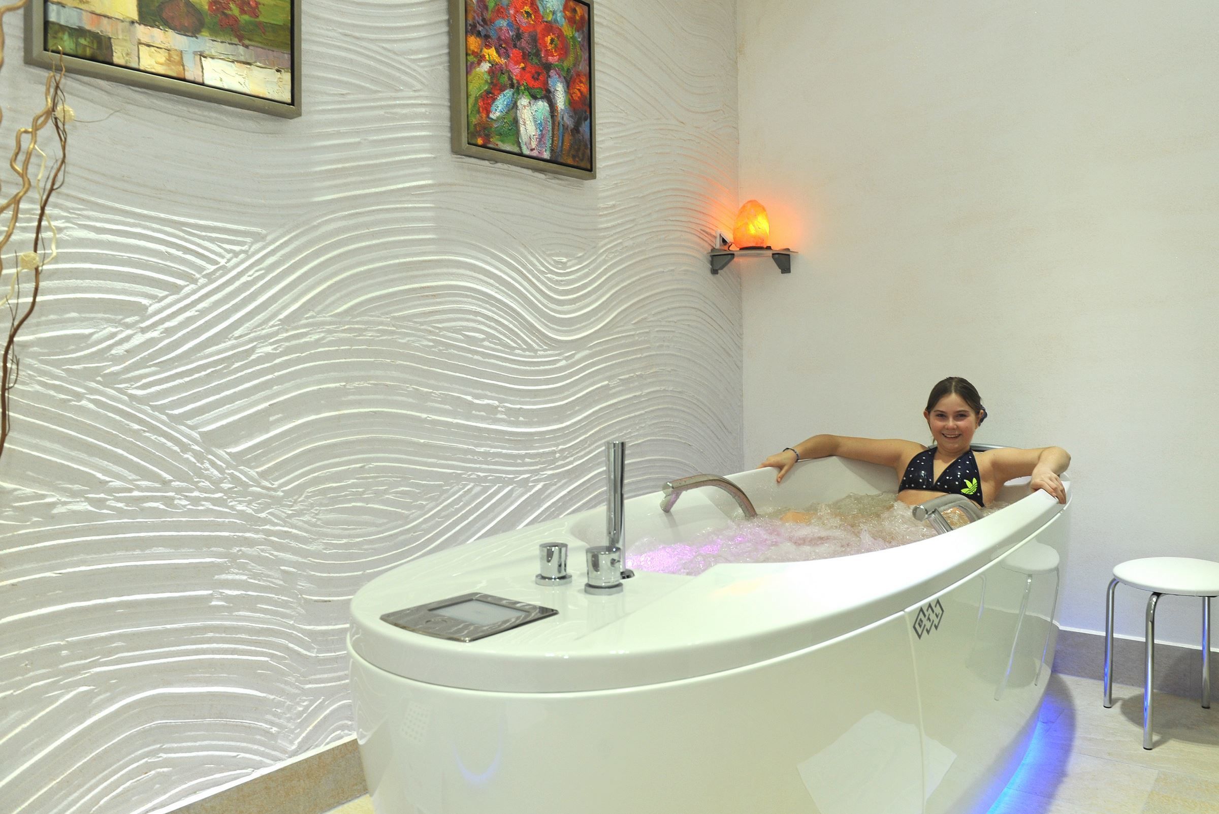 A modern bathroom with a large bathtub, a wall-mounted light, and decorative wall art.