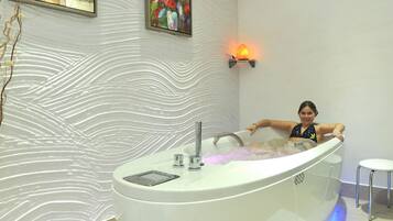A modern bathroom with a large bathtub, a wall-mounted light, and decorative wall art.