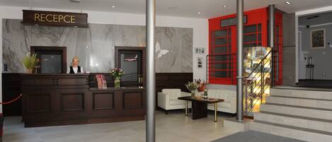 Zona de recepción de un hotel con un mostrador de mármol, una escalera de vidrio y detalles en rojo, y una decoración de diseño moderno.