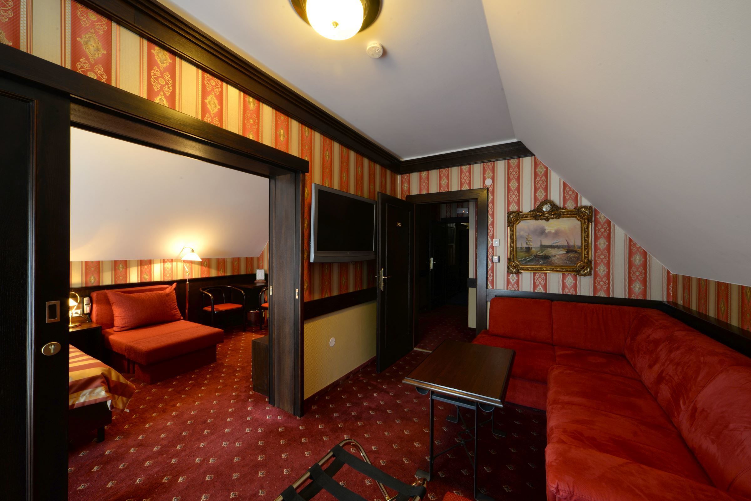 Habitación de hotel con alfombra roja, sofá, mesa, televisor y un cuadro en la pared.