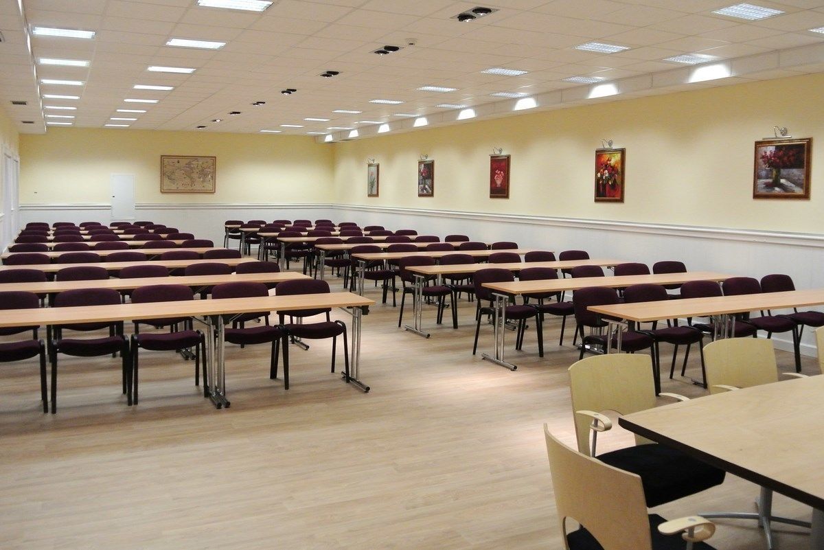 A conference room with rows of tables and chairs, a map on the wall, and framed pictures.