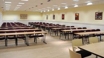 A conference room with rows of tables and chairs, a map on the wall, and framed pictures.