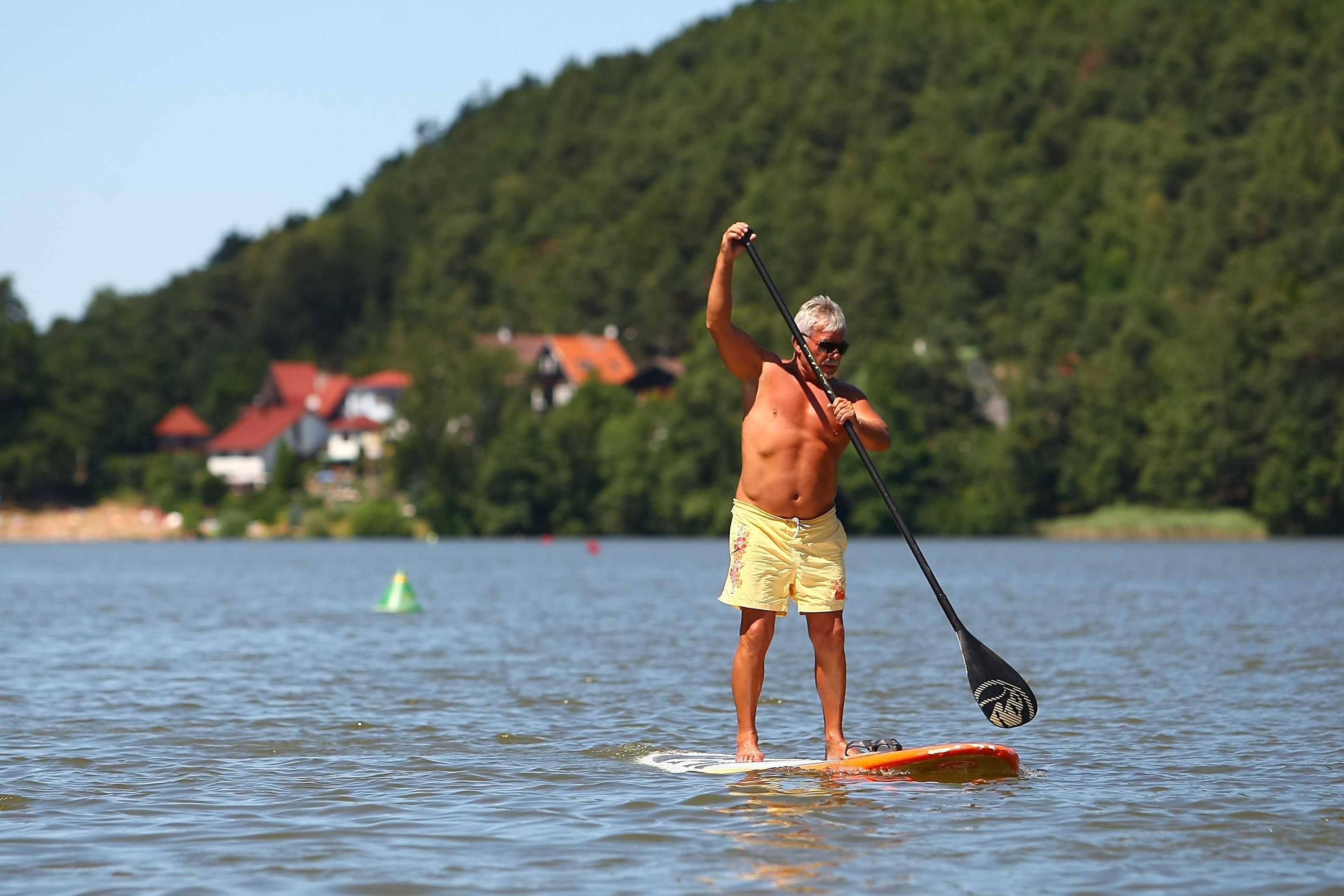 A person paddleboarding on a calm lake with a forested hill in the background.