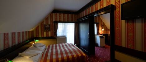 A hotel room with a bed, a desk, a chair, a TV, and a window with curtains.