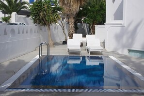 A rectangular swimming pool with a metal ladder, surrounded by white walls and a few palm trees. - Kymata Hotel (Santorini)
