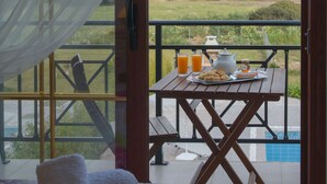 A balcony with a table set for breakfast, a bed with a colorful quilt, and a view of the sea. - Petra Villas (Rhodes)