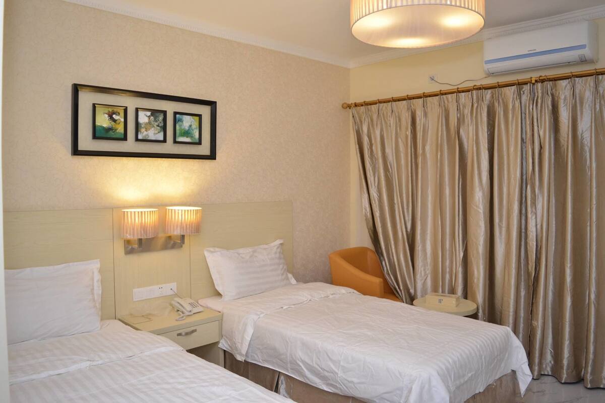 A hotel room with two beds, a nightstand with a phone, wall-mounted lights, a chair, and a curtain.