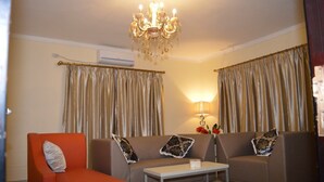 A living room with a sofa, armchair, and a coffee table. There is a chandelier, curtains, and a lamp. - Hotel Pacific (Nacala)
