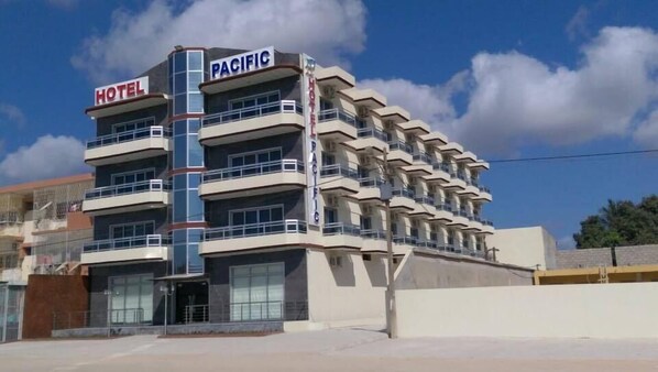 A multi-story hotel with a prominent 'PACIFIC' sign, featuring balconies on each floor and a modern architectural design.