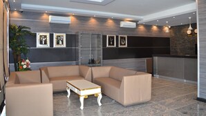 A modern lobby with a sectional sofa, a small white table, and framed artwork on the walls. - Hotel Pacific (Nacala)