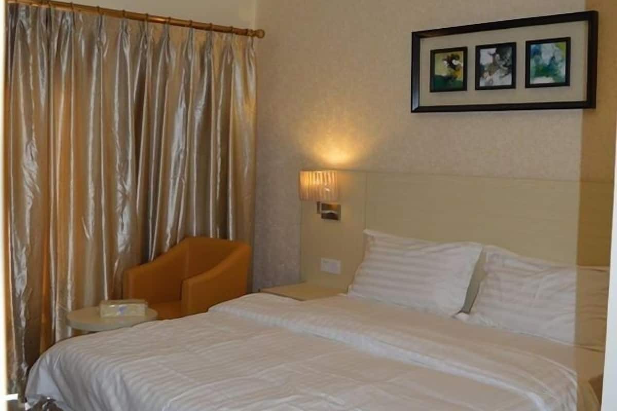 A hotel room with a bed, a chair, a lamp, and a curtain.
