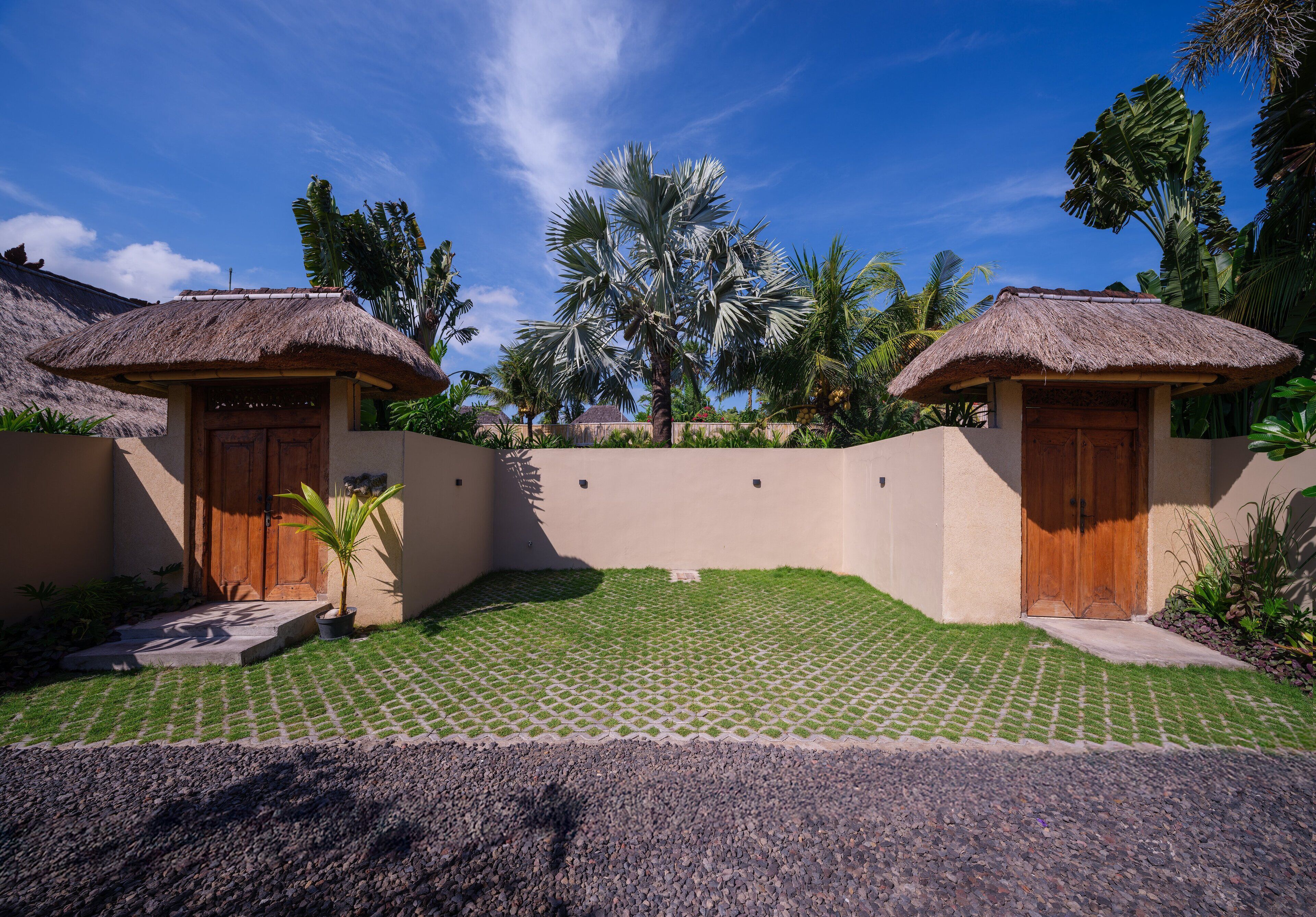 A resort with two thatched-roof cottages, a paved courtyard, and tropical vegetation.