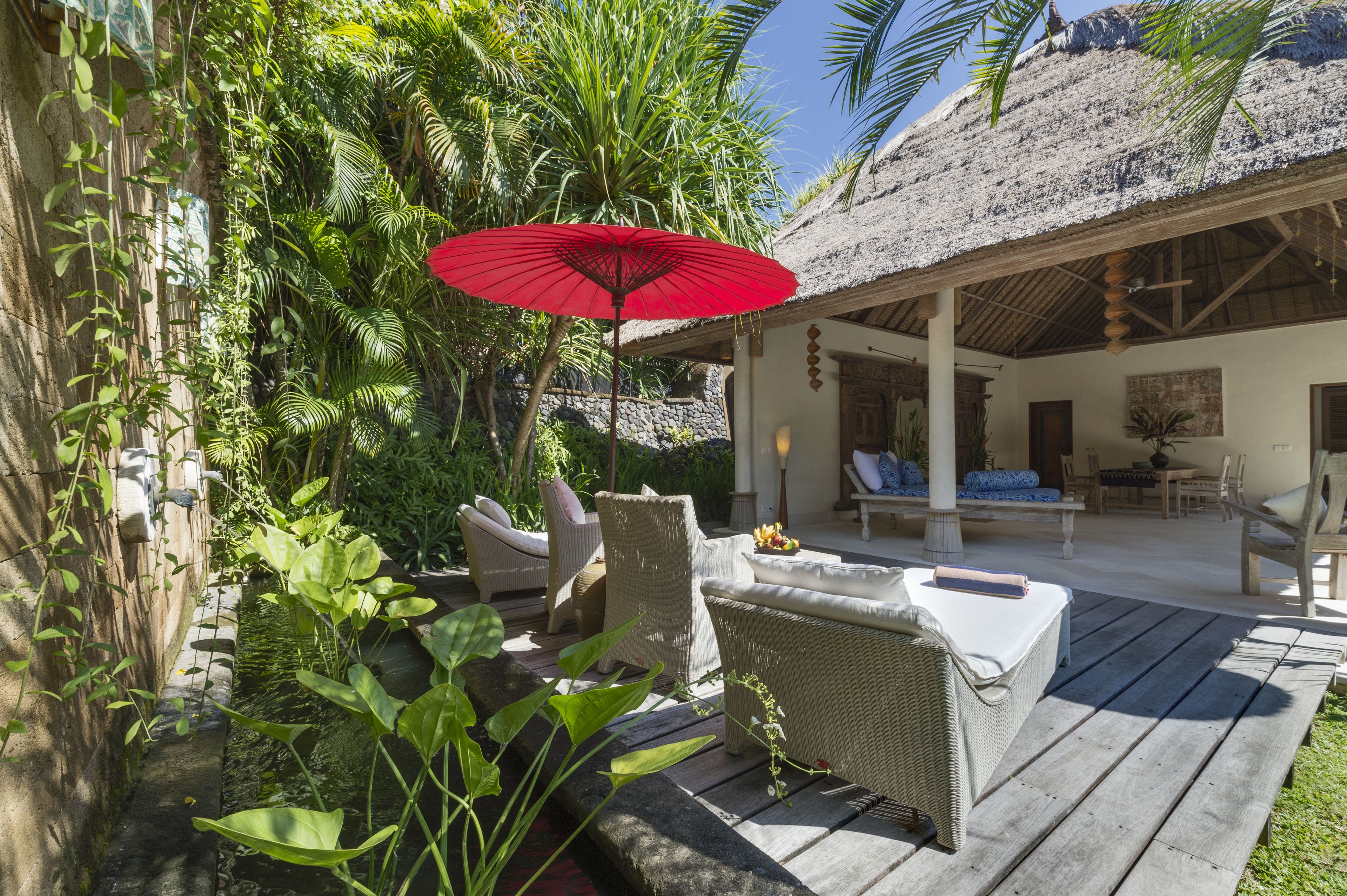 A wooden deck with wicker furniture, a red umbrella, and lush greenery.