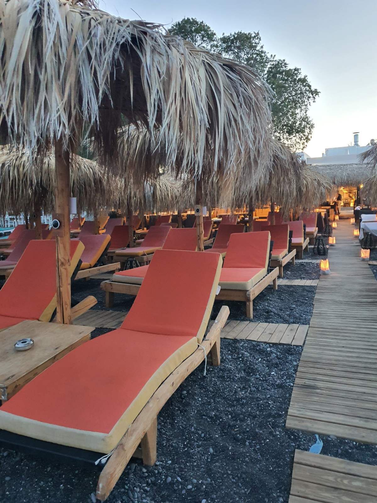 A beachside lounge area with wooden loungers and thatched umbrellas.