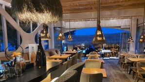 Un restaurant amb taules i cadires de fusta, llums penjants i una zona de bar amb ampolles i gots.