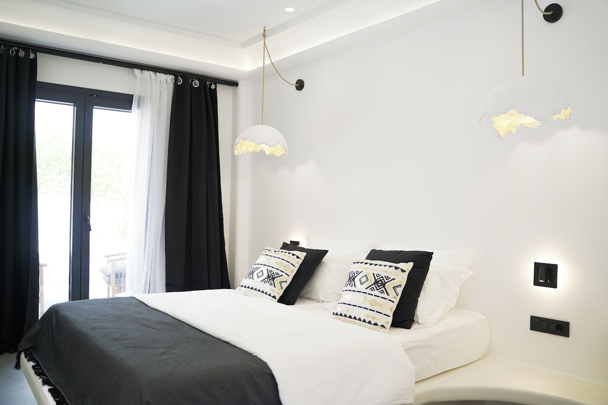 Une chambre à coucher moderne avec un lit, deux coussins décoratifs, une table de chevet et une fenêtre avec des rideaux.