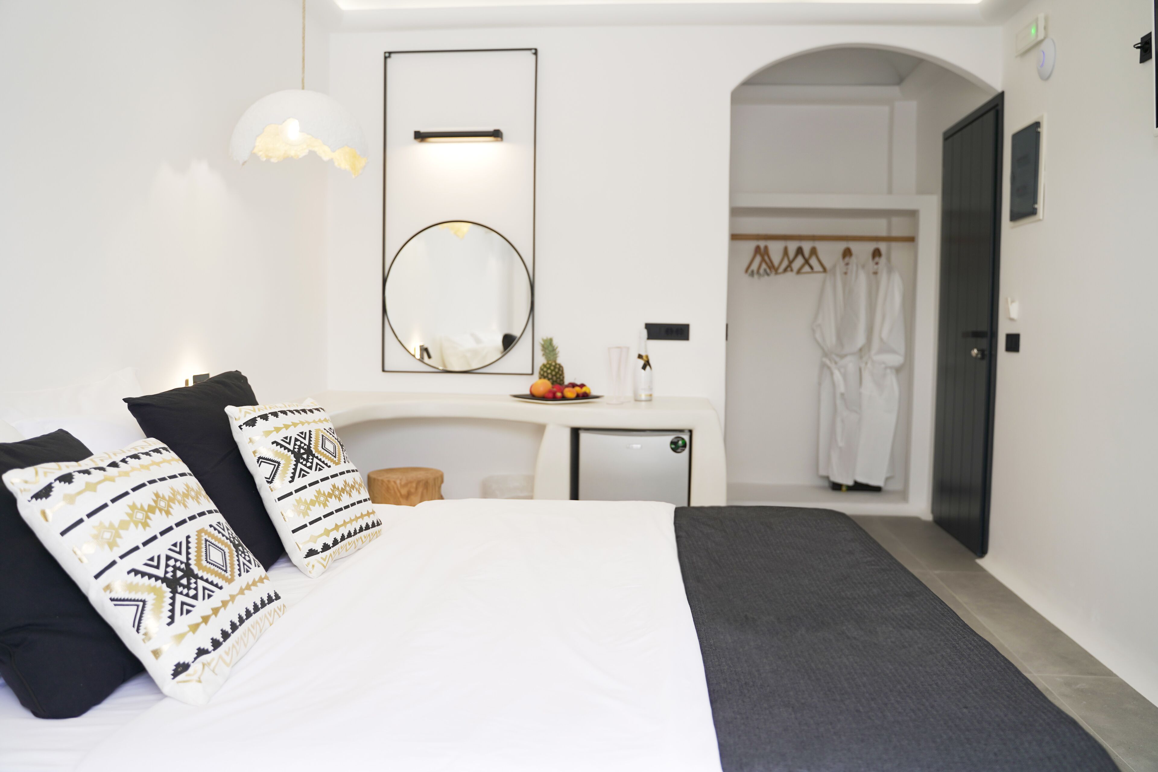 A modern hotel room with a bed, a desk, a mirror, and a wardrobe.