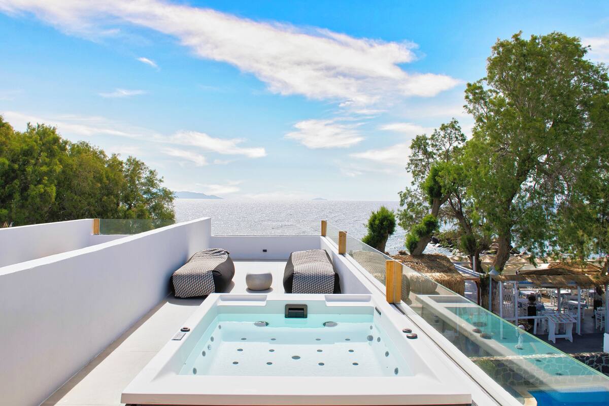 Terraza en la azotea con jacuzzi, sillas de descanso y balaustrada de cristal con vistas al mar.
