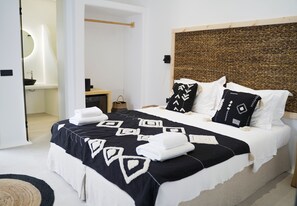 Un letto rifatto con cura, con una coperta a motivi decorativi, un comodino e una testiera fissata alla parete.