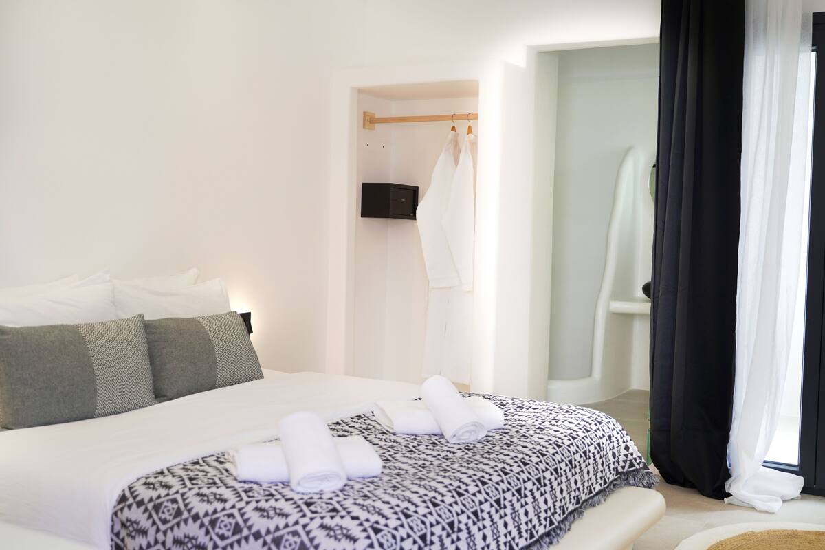 Habitación de hotel con una cama grande, una mesita de noche, una bata colgada y un baño visible a través de una puerta abierta.
