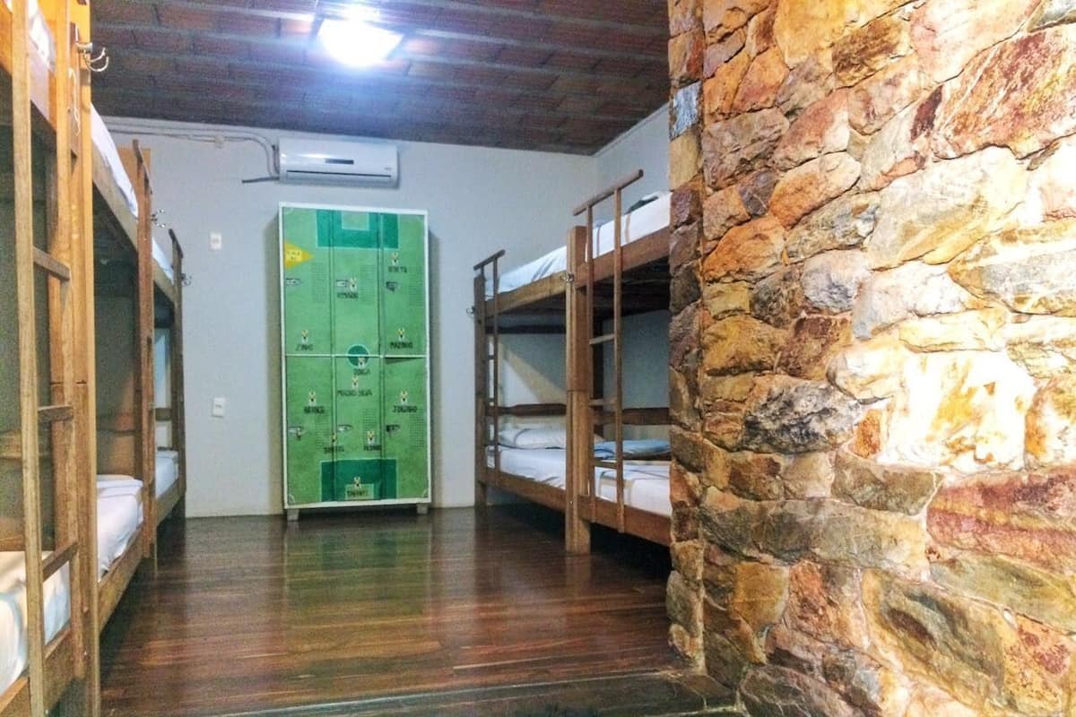 Quarto com beliches, um armário verde e uma parede de pedra.