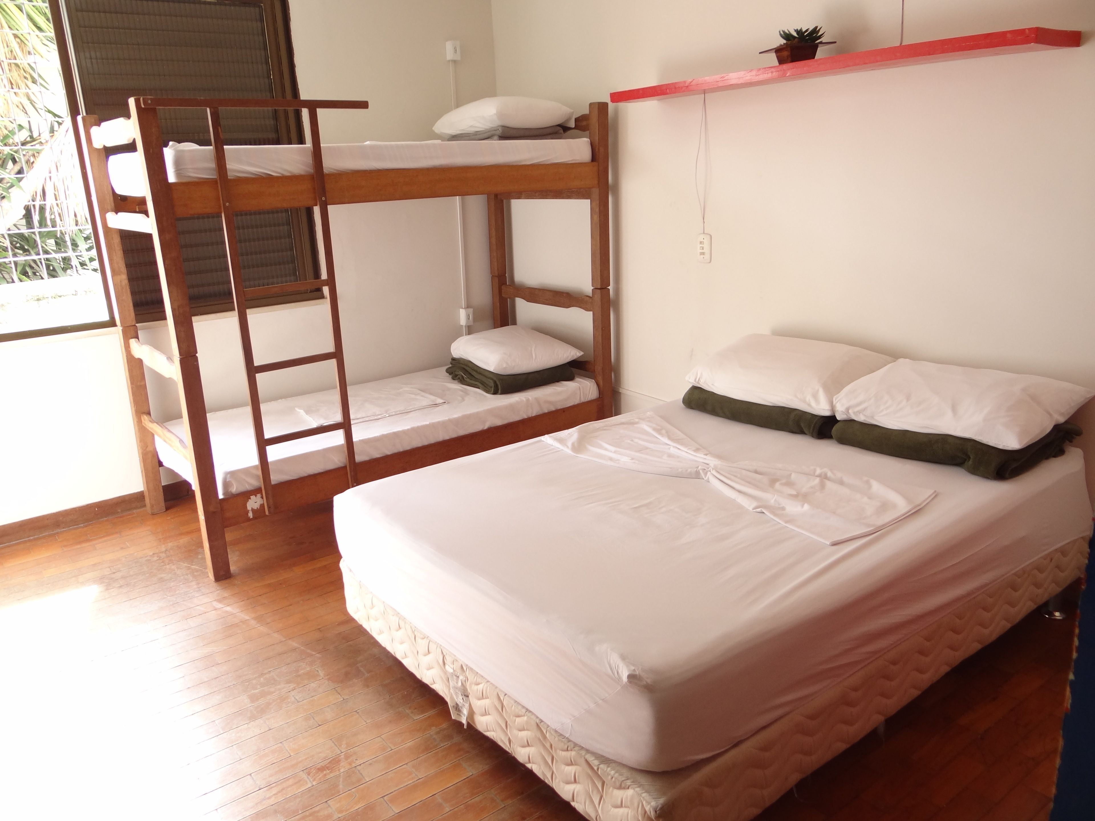 Quarto com beliche, uma escada de madeira, uma cama de solteiro e uma prateleira sobre a cama.