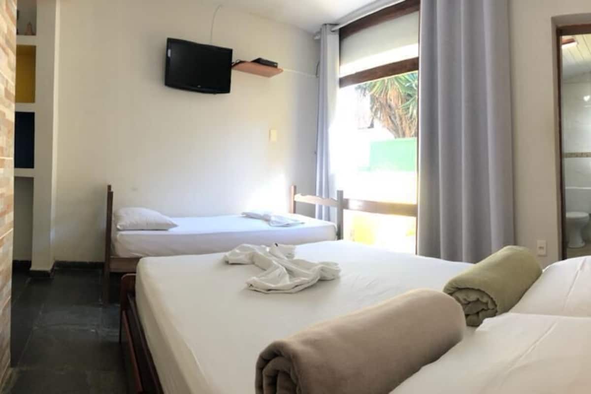 Quarto de hotel com duas camas, uma TV fixada na parede e vista para o exterior através de uma janela.