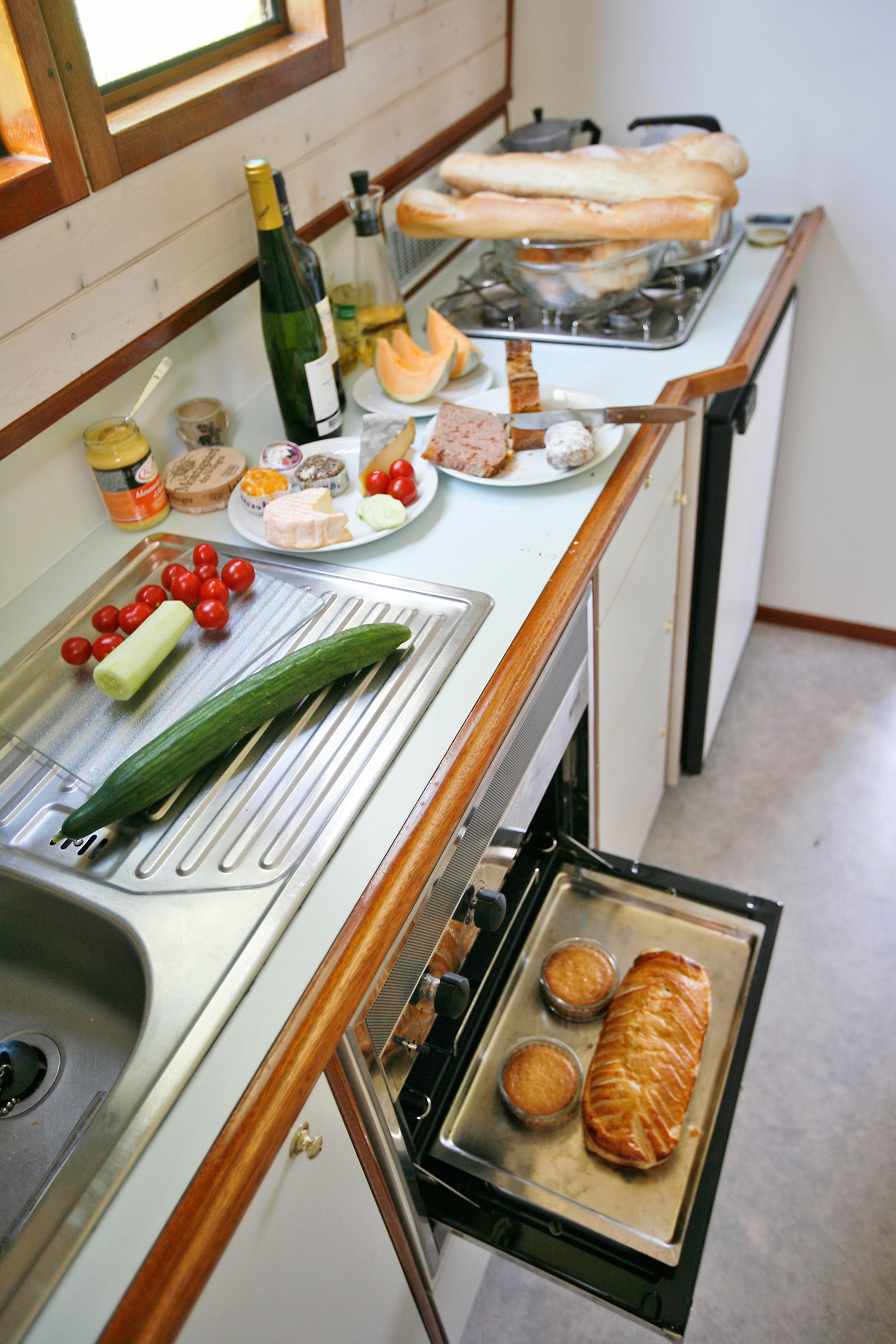 A kitchen with a sink, a stove, and various food items and condiments on the counter.
