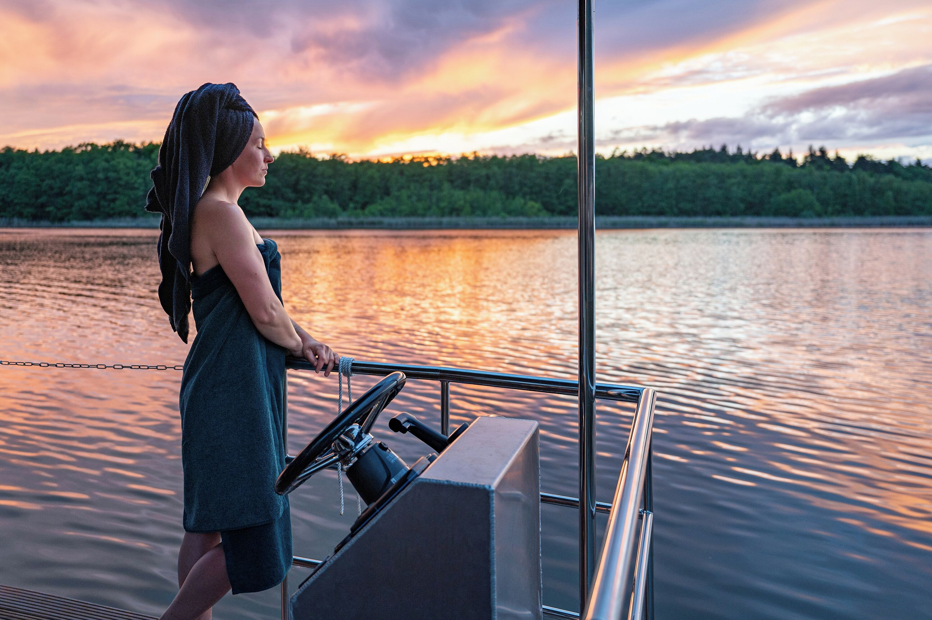 A person on a boat steering, with a calm lake and trees in the background.