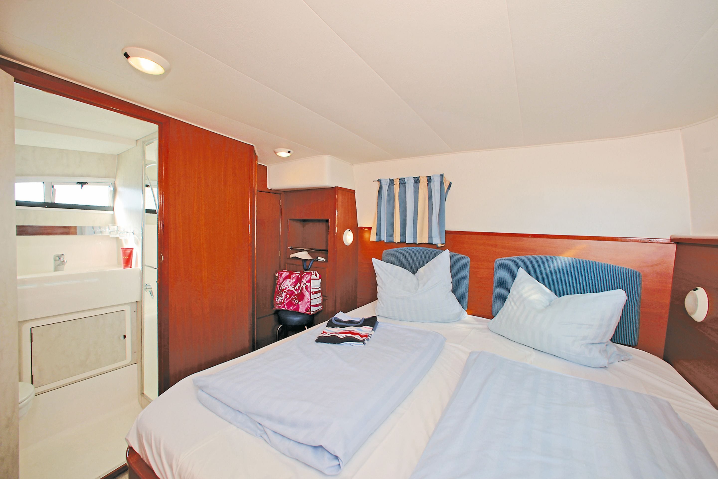 A hotel room with a bed, a wooden headboard, a window with curtains, and a bathroom visible through an open door.