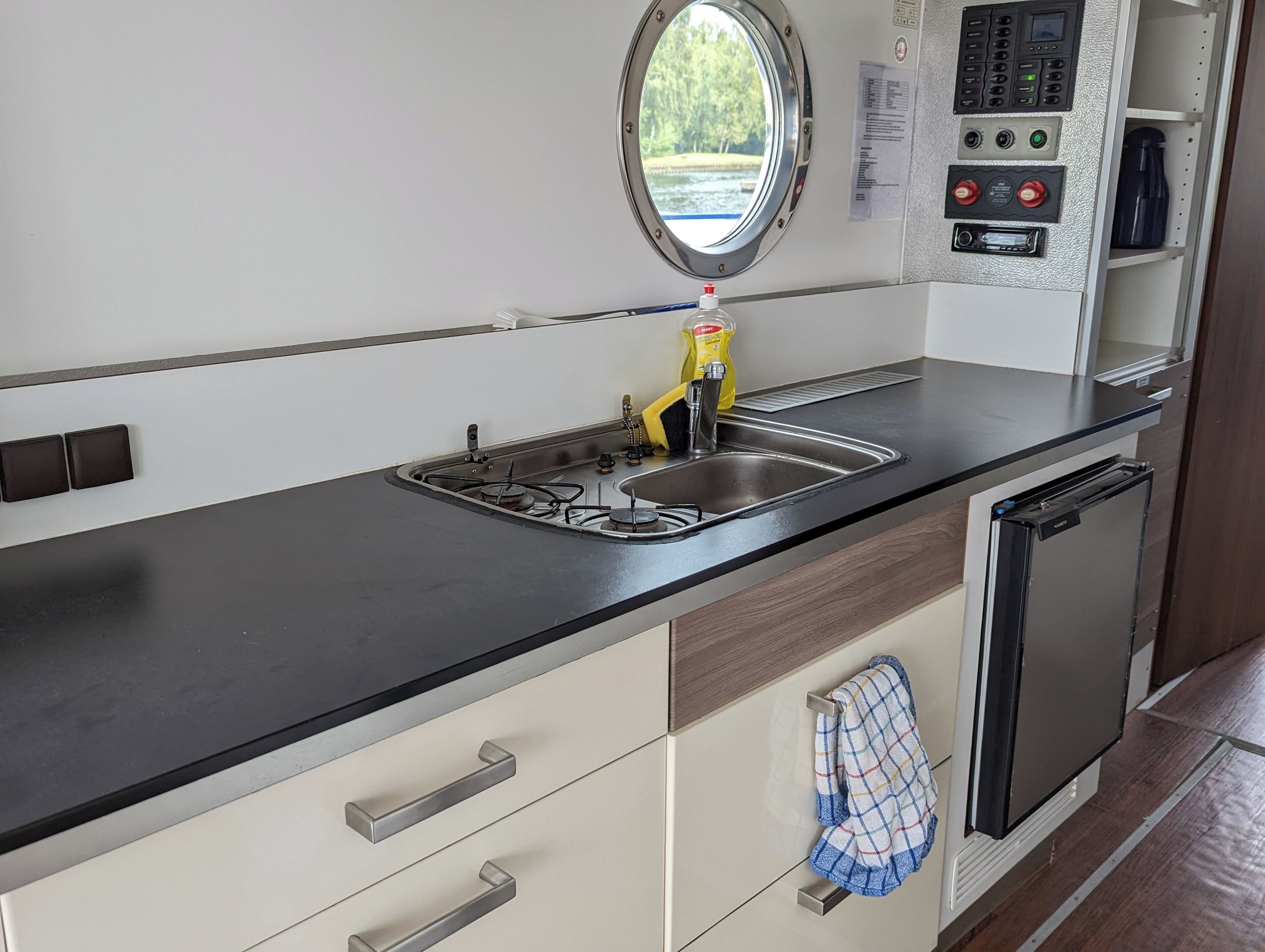 A modern kitchen with a black countertop, stainless steel sink, and a window above the sink.
