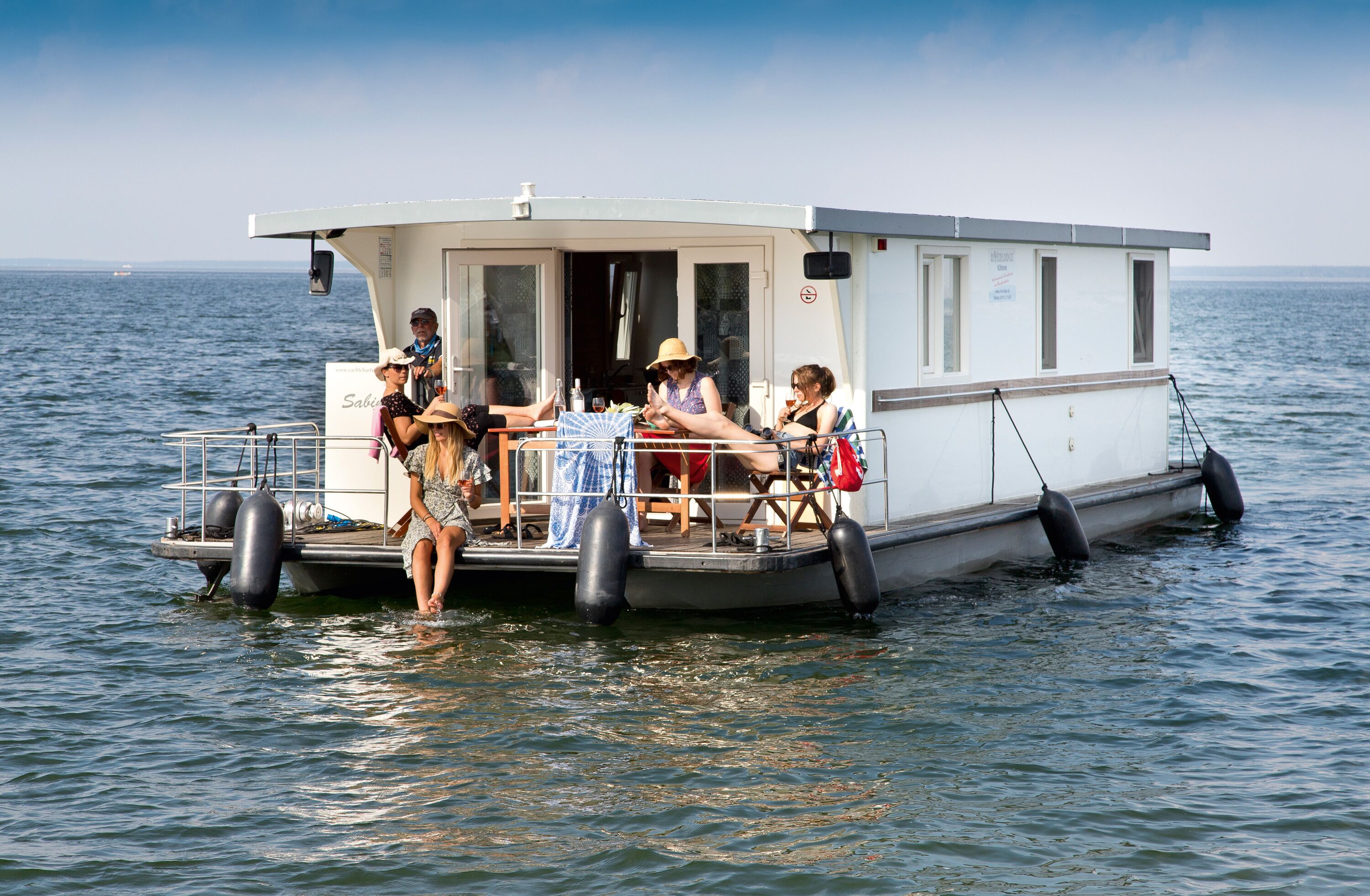 A boat with a covered deck, a table with chairs, and people sitting and standing.