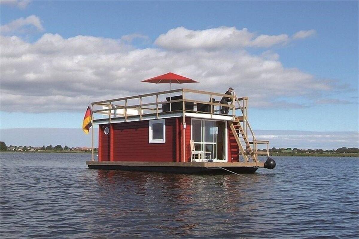 A red houseboat with a deck, windows, and a red umbrella.