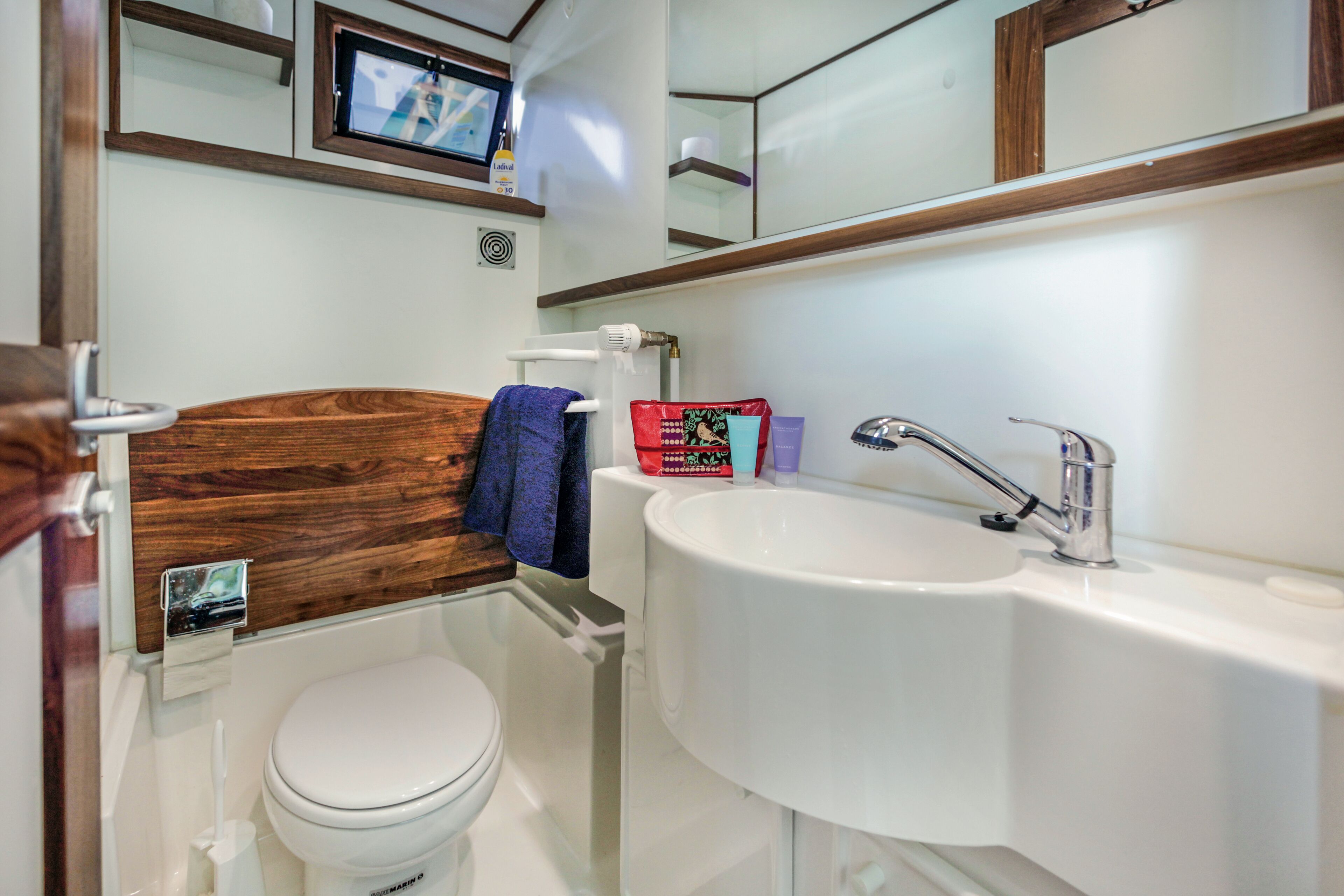 A bathroom with a wooden headboard, a white toilet, a sink with a faucet, and a mirror above the sink.