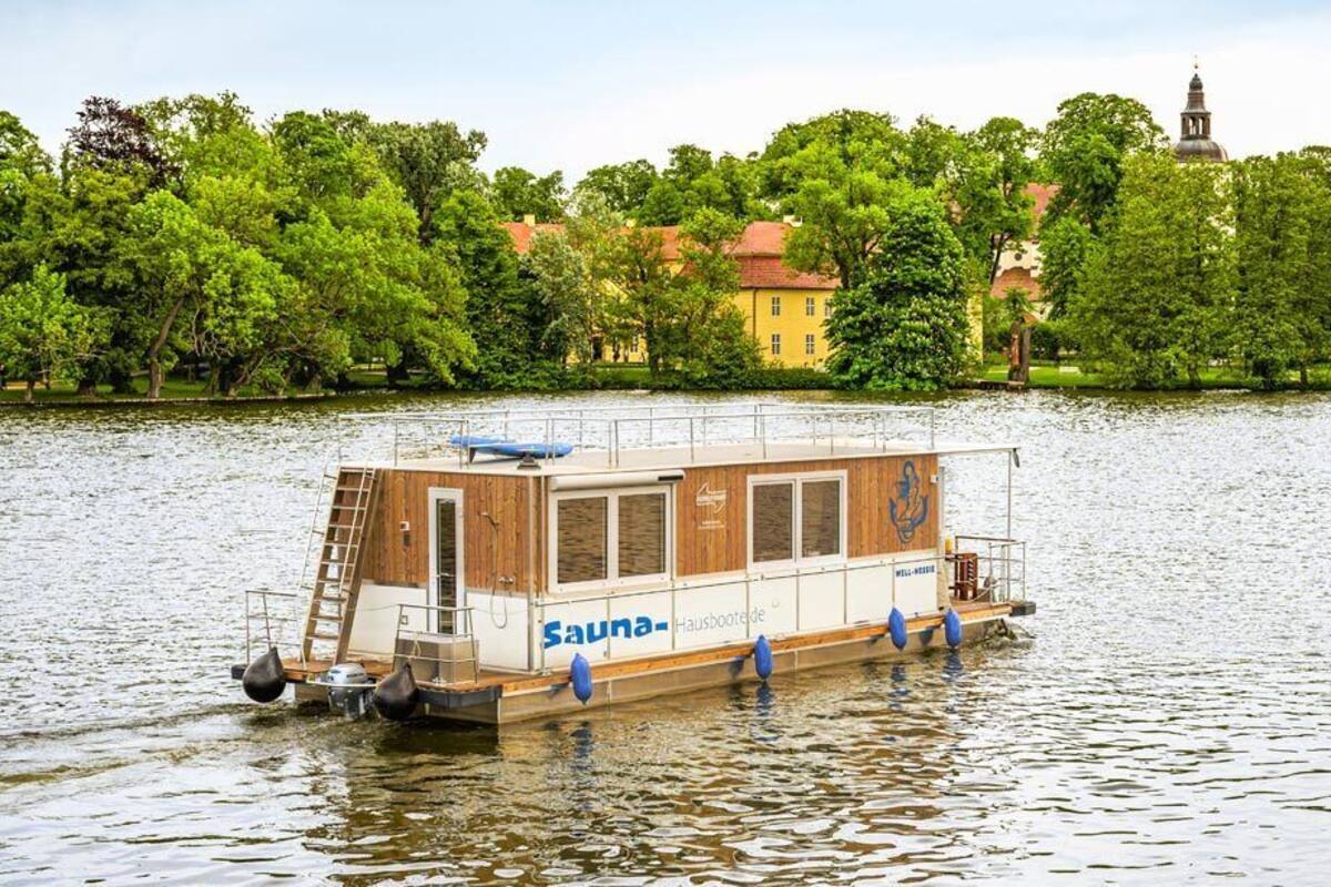 A houseboat with a wooden deck and a ladder, floating on a calm river.