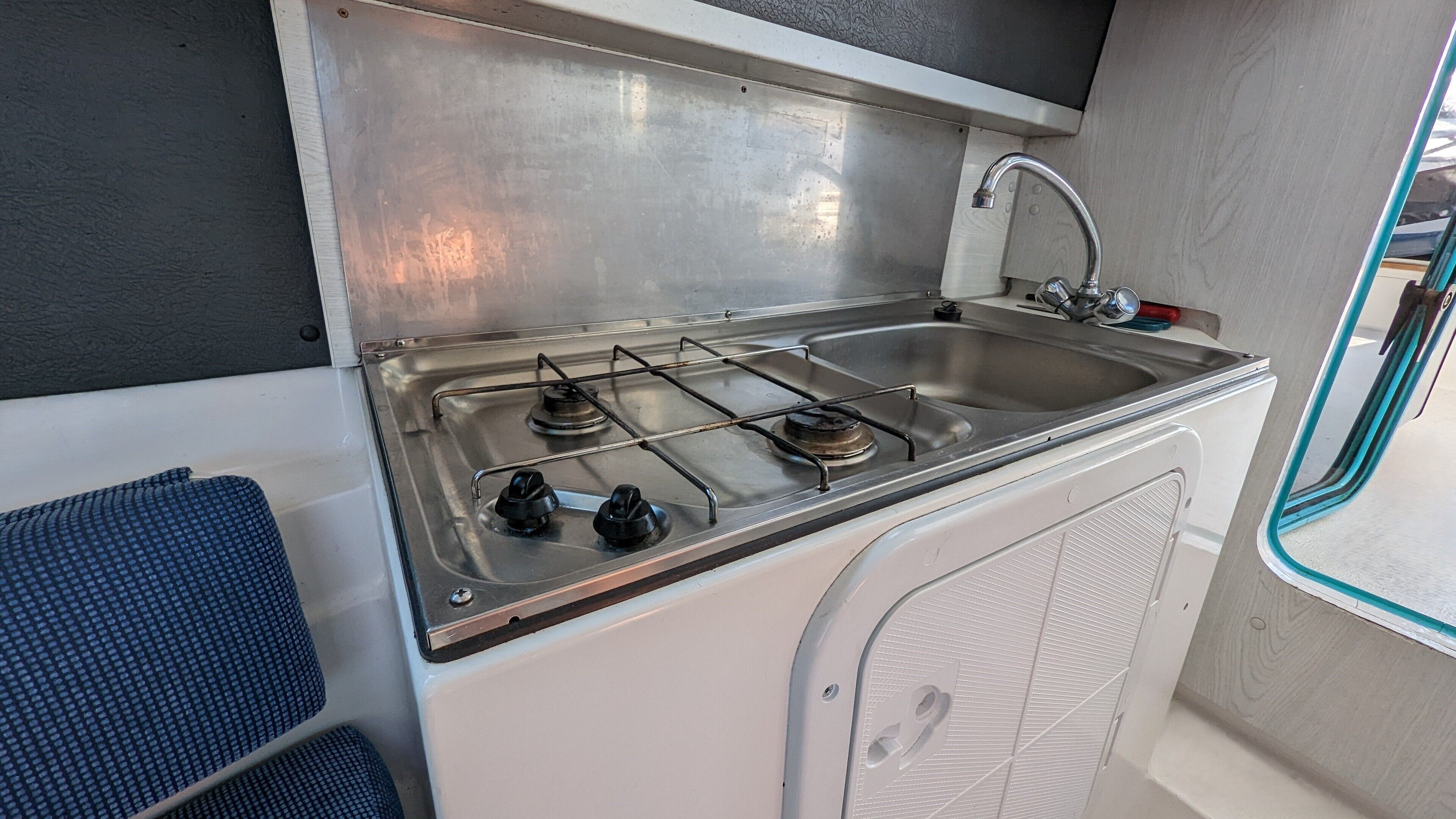 Una kitchenette compacta con estufa a gas, lavamanos y un ventanal pequeño.