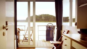 Una habitación con puerta corredera que da a un balcón con vistas a un lago y árboles.