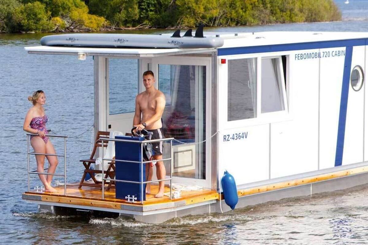 A cabin on a boat with a small deck, a steering wheel, and a person standing on the deck.
