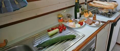 A kitchen with a sink, a cutting board, a variety of food items, and a bottle of wine.