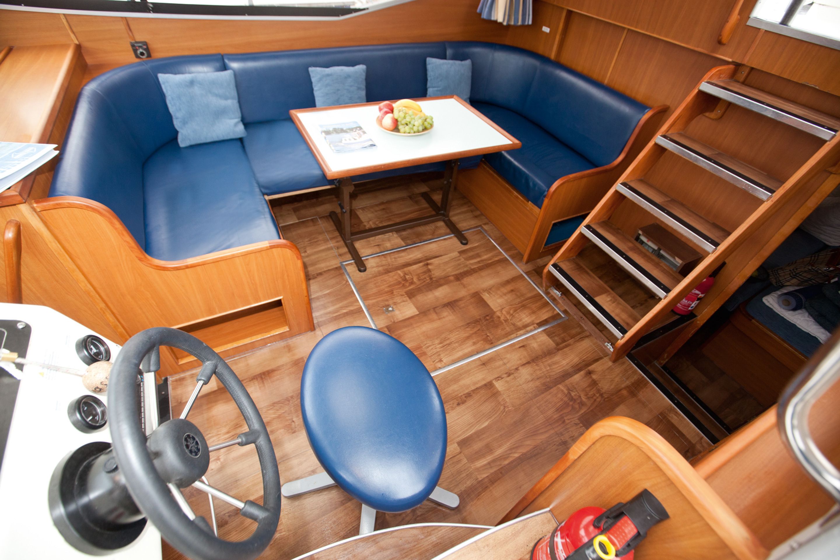 Ein kompakter Wohnraum mit einem blauen Sofa, einem kleinen Tisch mit Obstschale, einem Lenkrad und einem Holzschrank.