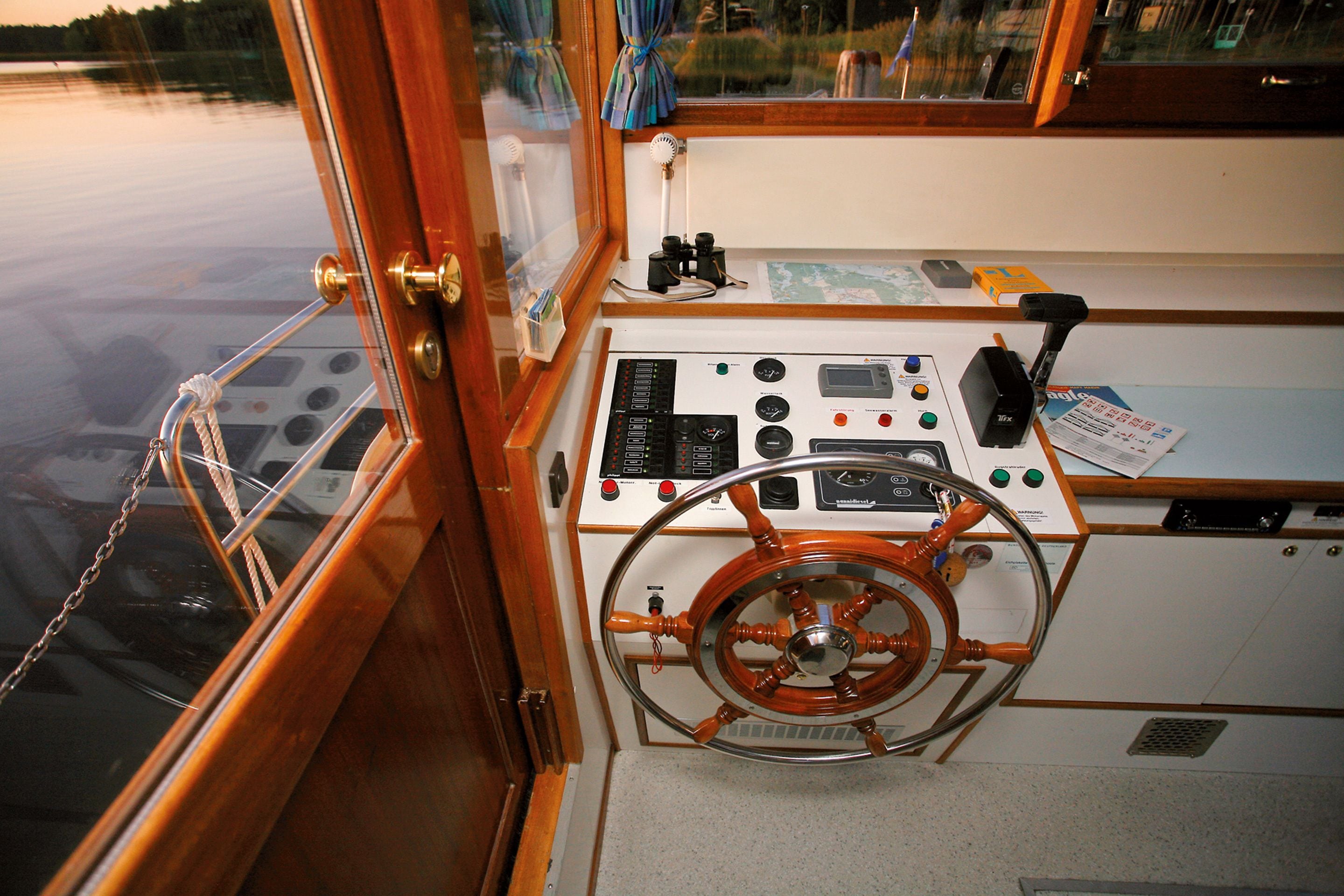 Un poste de pilotage de bateau, équipé d’un volant, de divers panneaux de commande et d’une fenêtre donnant sur l’eau.